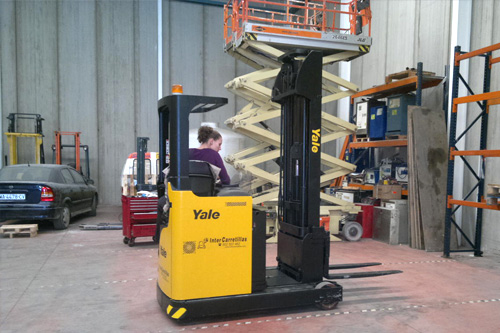 Operaria en almacén trabajando con apilador eléctrico.