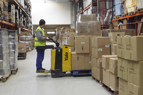 Trabajador realizando trabajo de colocación de mercancía en almacén con transpaleta eléctrica.