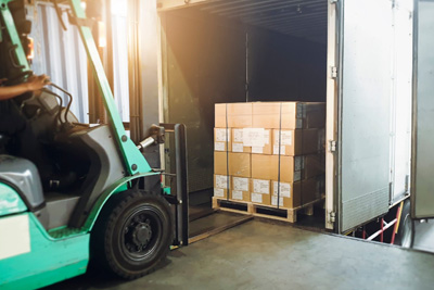 operario cargando un camión con carretilla elevadora en almacén.
