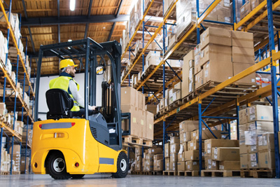 Carretillero realizando maniobras en almacén lleno de mercancía. 